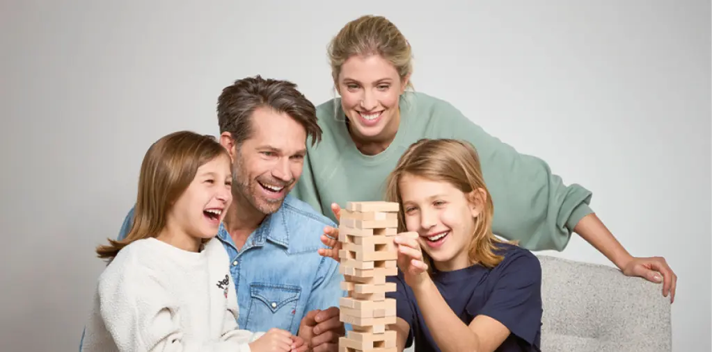 Glückliche Familie spielt gemeinsam ein Geschicklichkeitsspiel am modernen Esstisch. Eltern und Kinder lachen und verbringen Zeit zusammen. Wohnliche Atmosphäre mit hochwertigem Tisch und gemütlichem Zuhause Ambiente.